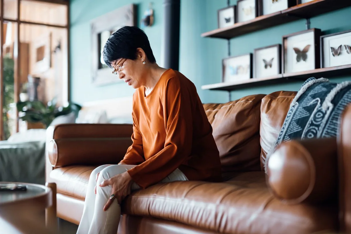 a-distraught-senior-asian-woman-feeling-unwell-suffering-from-pain-in-leg-while-sitting-on-sofa-in-the-living-room-at-home
