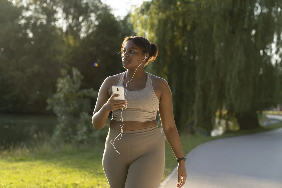 african-american-woman-using-mobile-phone-and-earphones-during-the-walking-at-the-park-in-a-summer-day