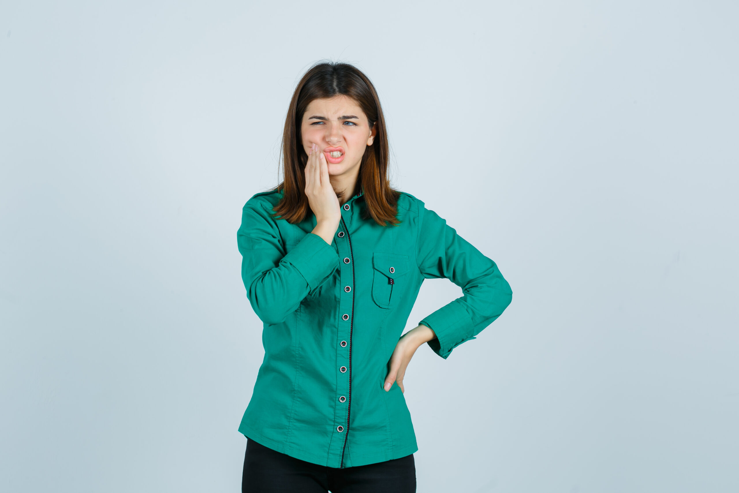 young female suffering from toothache in green shirt and looking painful. front view